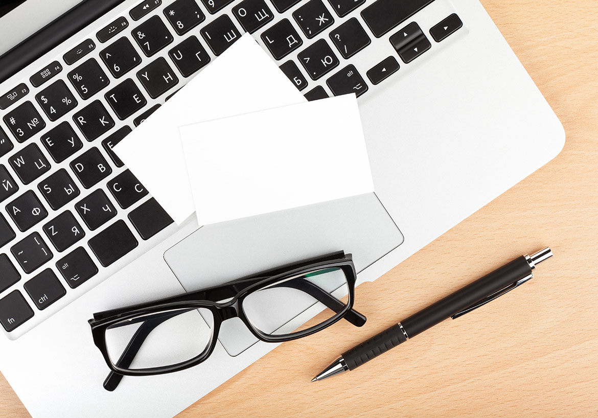 aerial view of apple laptop keyboard with notepad, reading glasses and pen